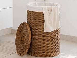 Hoher brauner Rattan-Wäschekorb mit hellem Innenbeutel und beigem Tuch im Badezimmer, der Deckel steht davor