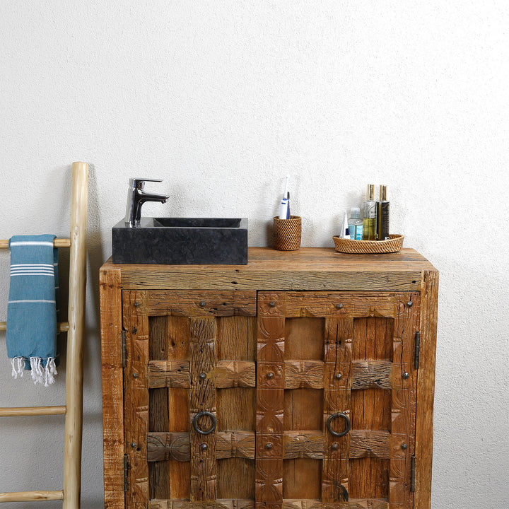 Eckiges Aufsatzwaschbecken aus Marmor mit dunkler Maserung auf rustikalem Holzwaschtisch, kombiniert mit verchromter Armatur und natürlichen Accessoires vor heller Wand